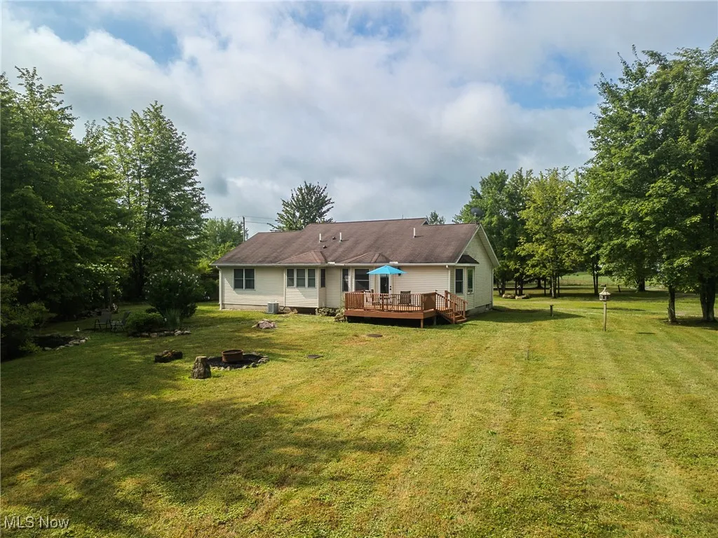 Back of house featuring a wooden deck, a lawn, and an outdoor fire pit