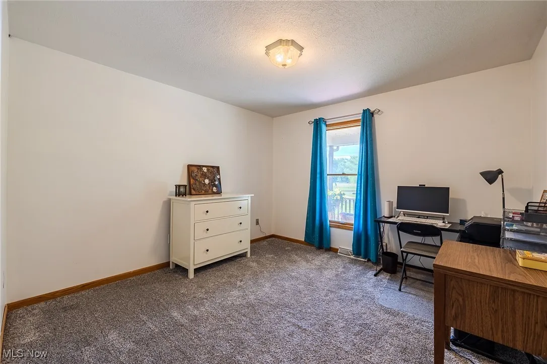 Bedroom currently being used as a home office, carpeted, with a textured ceiling.
