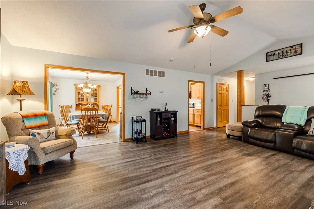 Living room featuring lofted ceiling, dark wood-style flooring, a ceiling fan, and a chandelier