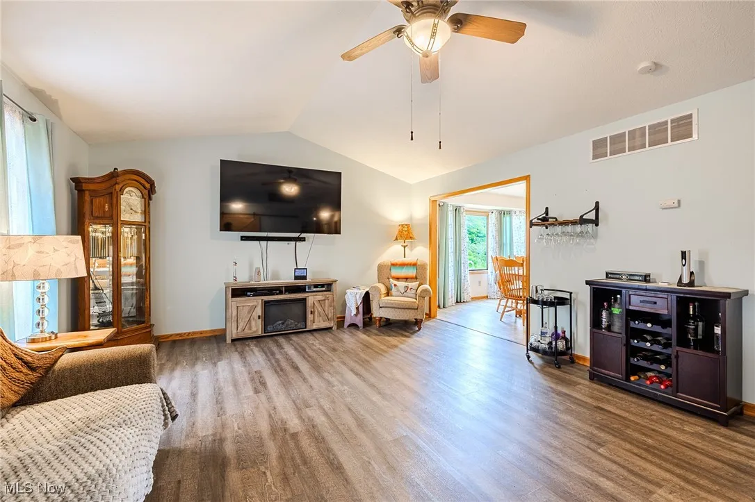 Living room with wood finished floors, vaulted ceiling, and a ceiling fan