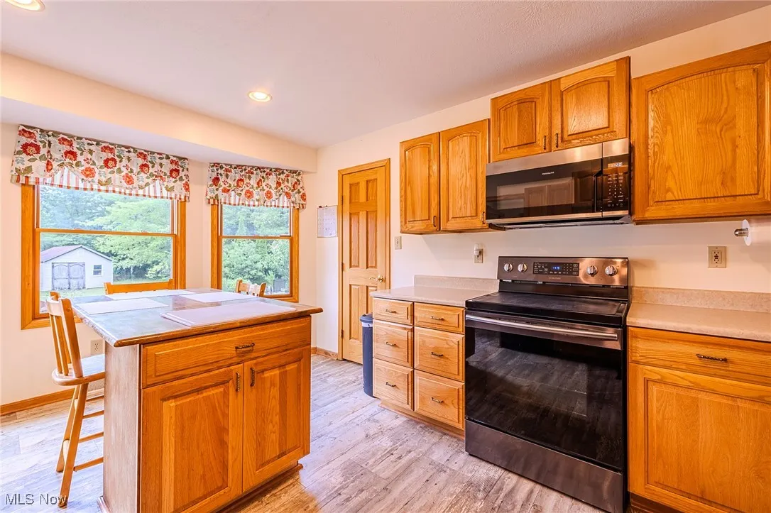 Kitchen featuring electric range oven, stainless steel microwave, light countertops, light wood-type flooring, and recessed lighting