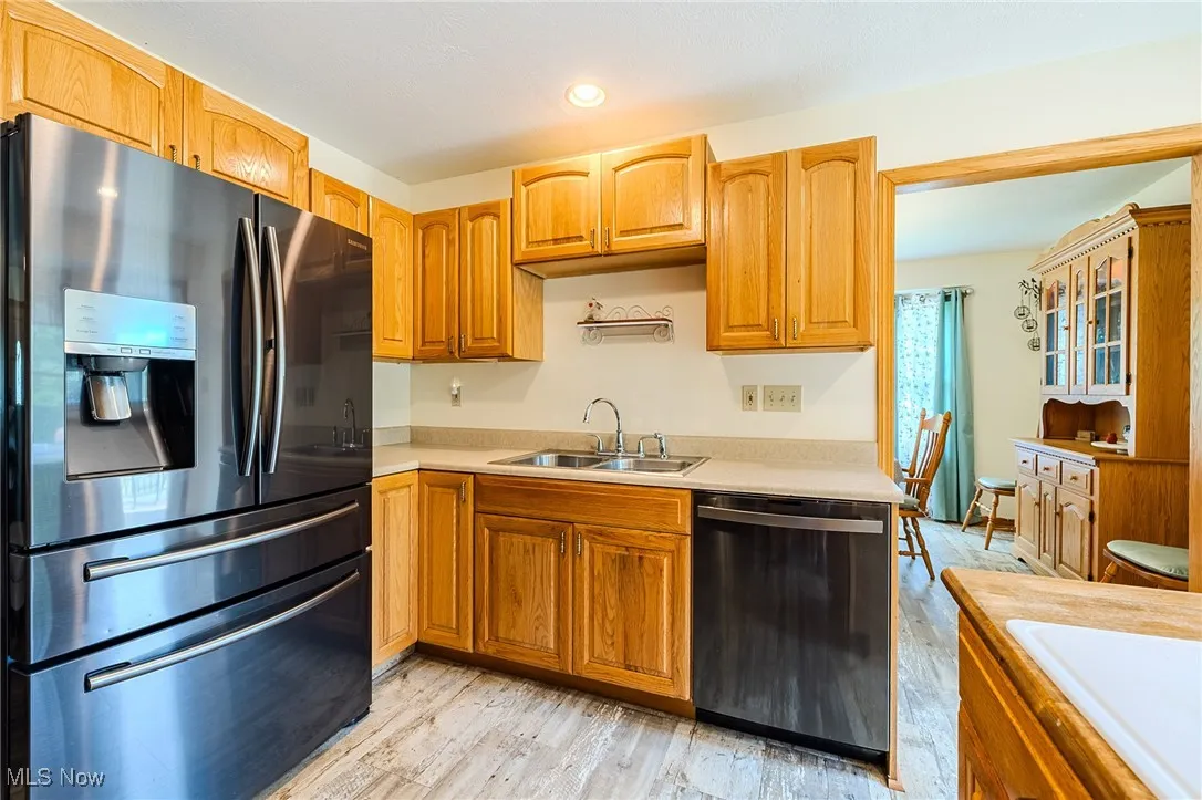 Kitchen with stainless steel fridge, dishwashing machine, light countertops, and light wood finished floors