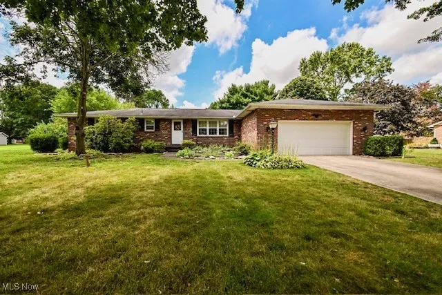 Single story home featuring concrete driveway, an attached garage, brick siding, and a front lawn