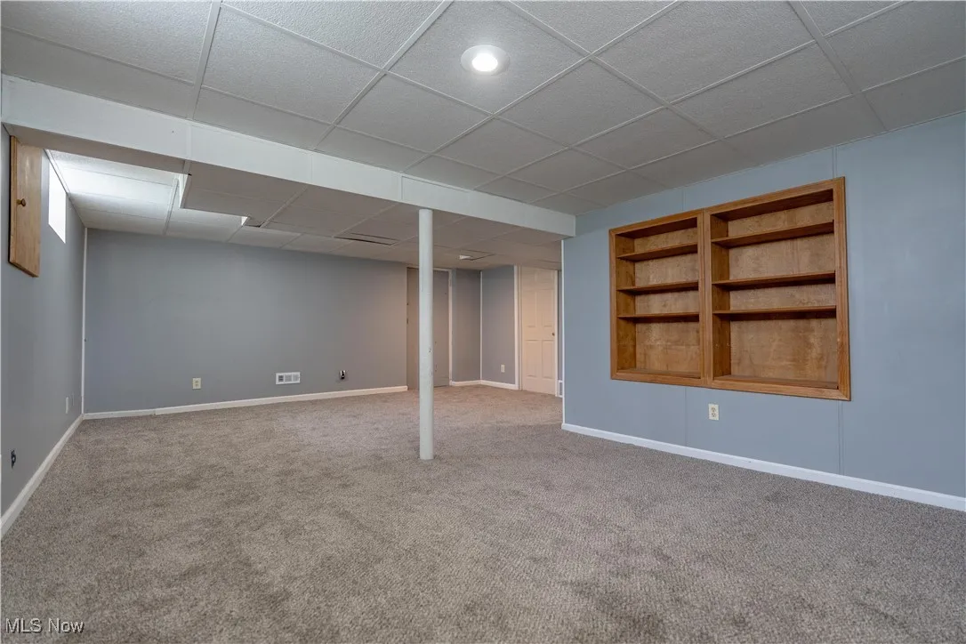 Finished basement with a drop ceiling, carpet floors, and built in features