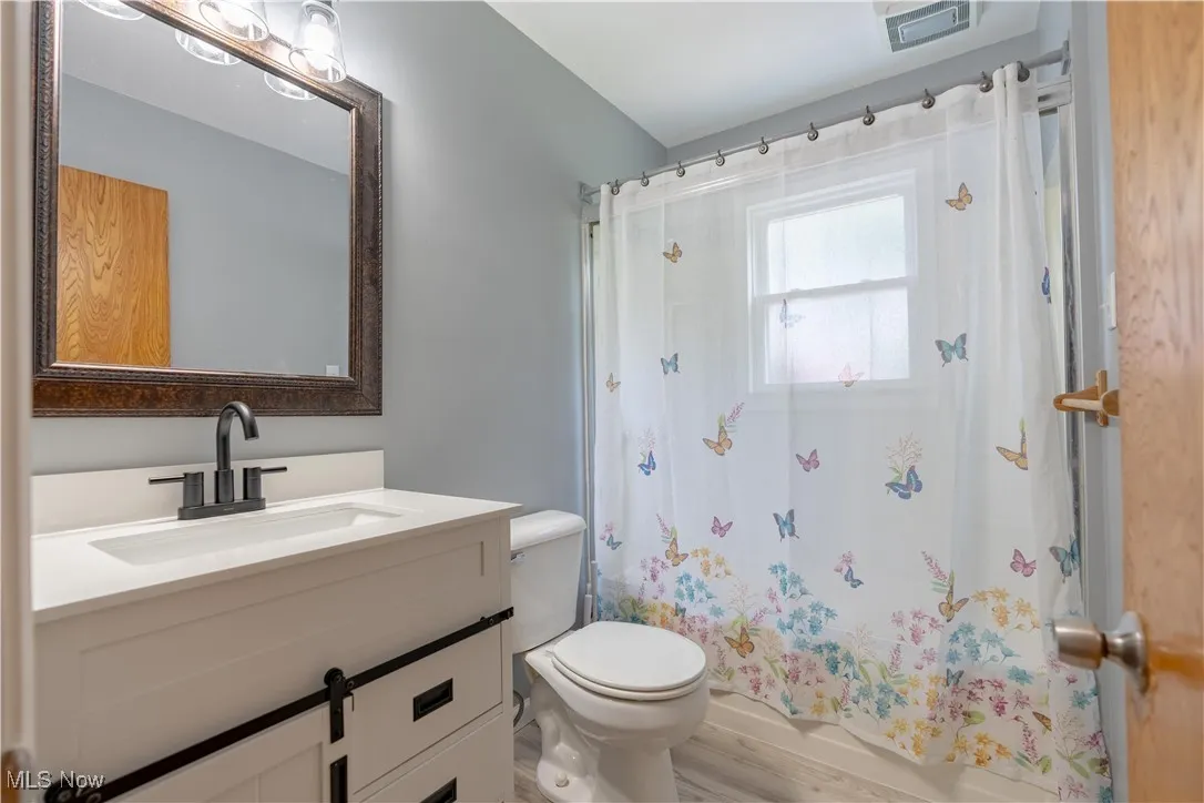 Bathroom with vanity, wood finished floors, and shower / tub combo with curtain
