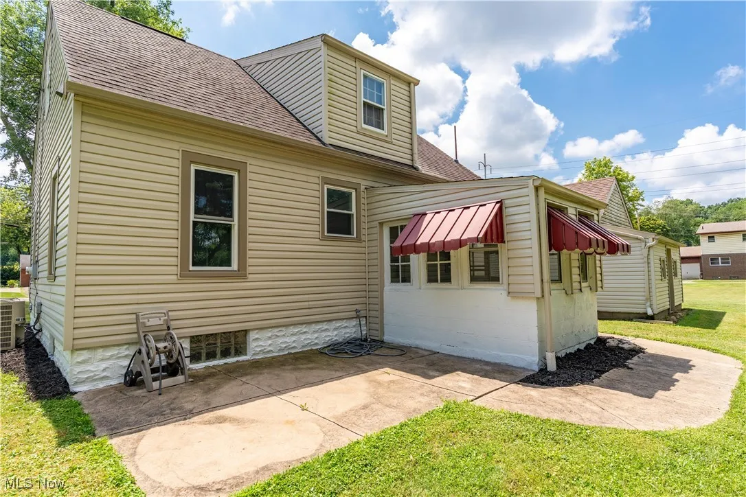 Back of property with roof with shingles, a lawn, and a patio area