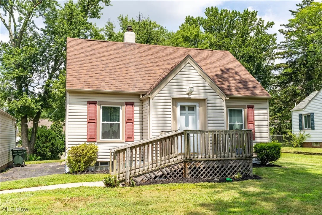 View of front of property featuring a shingled roof, a front lawn, a chimney, and a wooden deck