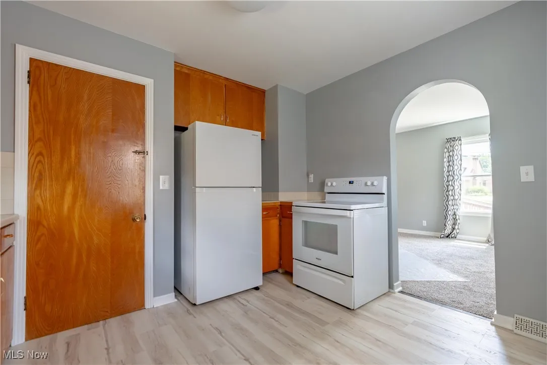 Kitchen featuring white appliances, light wood finished floors, arched walkways, brown cabinets, and light countertops