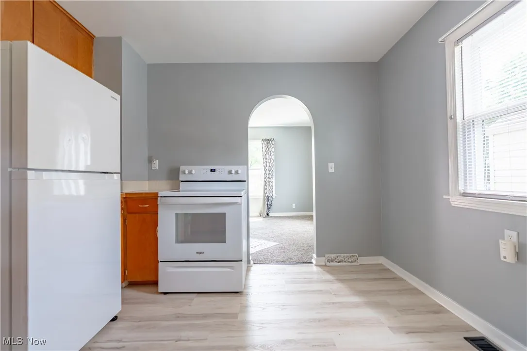 Kitchen featuring white appliances, arched walkways, brown cabinets, and light countertops