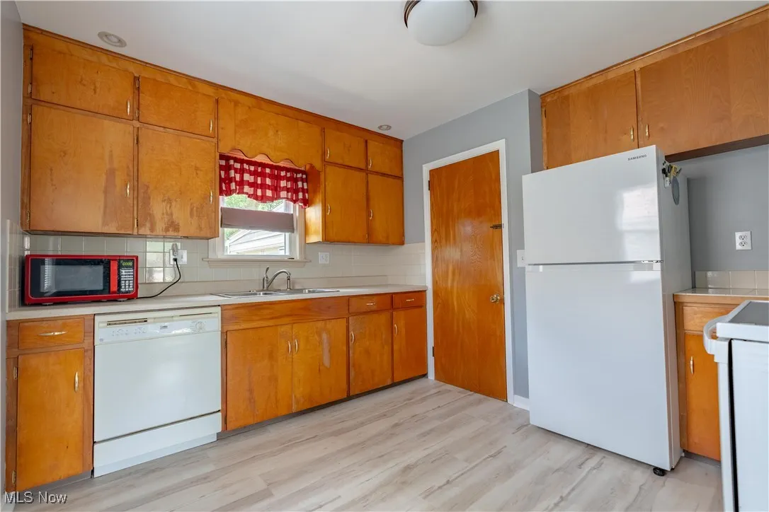 Kitchen with white appliances, brown cabinetry, light countertops, and tasteful backsplash