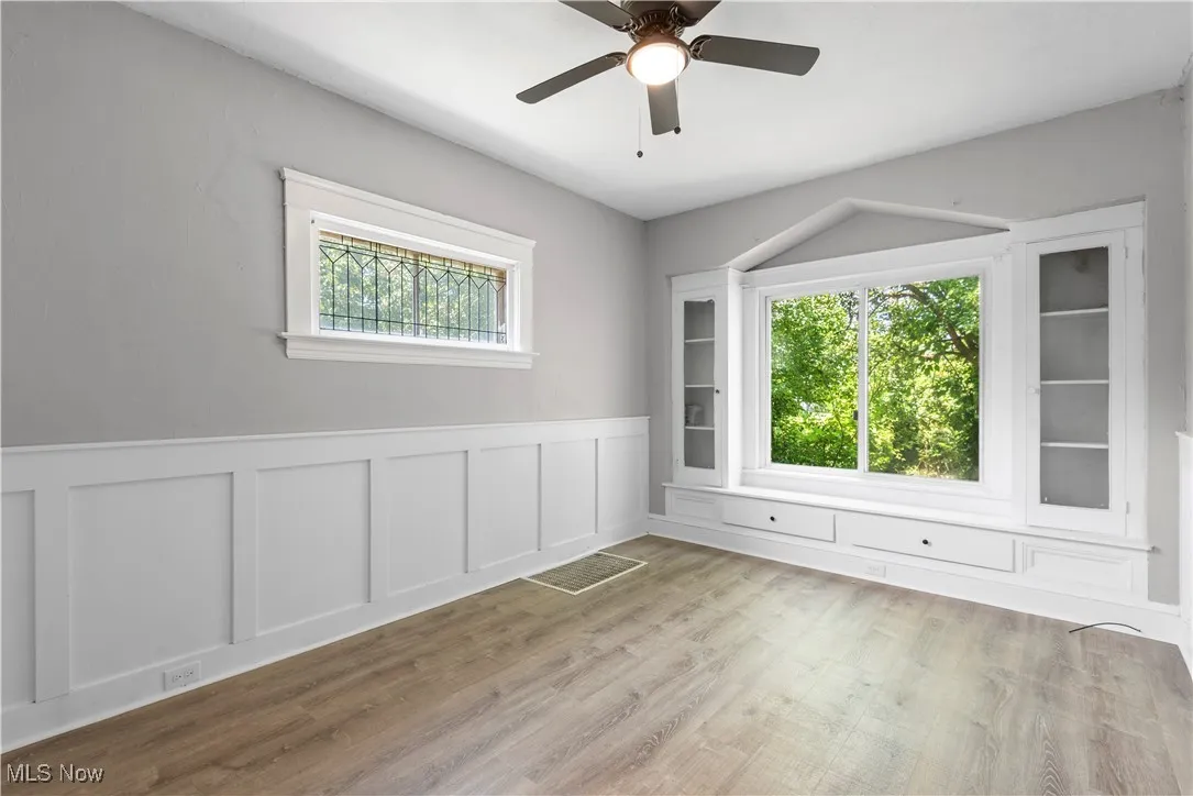 Spare room featuring a decorative wall, wainscoting, wood finished floors, and ceiling fan