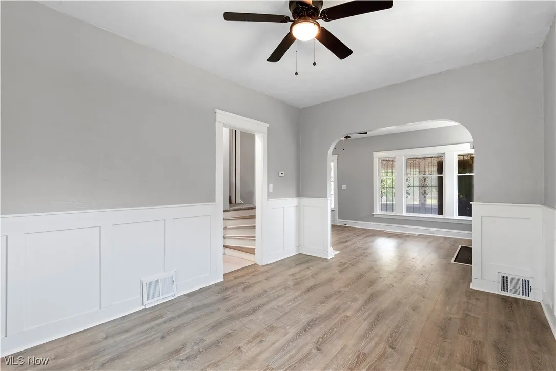 Unfurnished room featuring arched walkways, a wainscoted wall, a decorative wall, ceiling fan, and wood finished floors