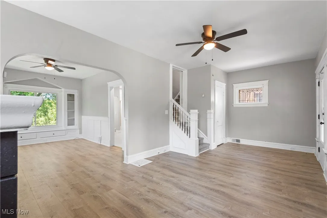 Unfurnished living room with a ceiling fan, arched walkways, wood finished floors, stairs, and a wainscoted wall