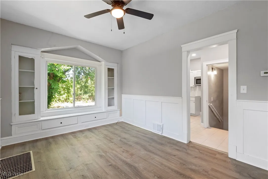 Unfurnished room featuring wainscoting, a decorative wall, a ceiling fan, and wood finished floors
