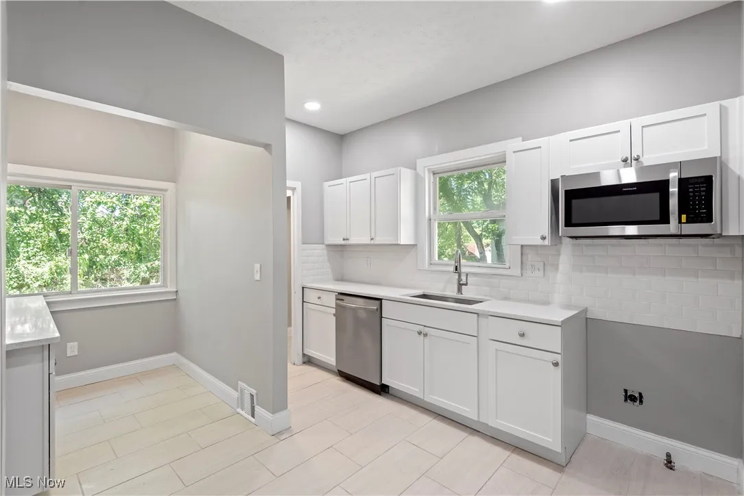 Kitchen featuring appliances with stainless steel finishes, light countertops, backsplash, white cabinets, and recessed lighting