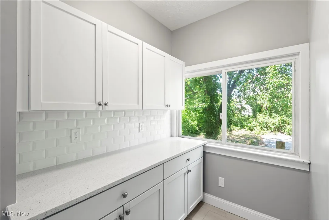 Kitchen with plenty of natural light, white cabinets, light stone countertops, backsplash, and a textured ceiling