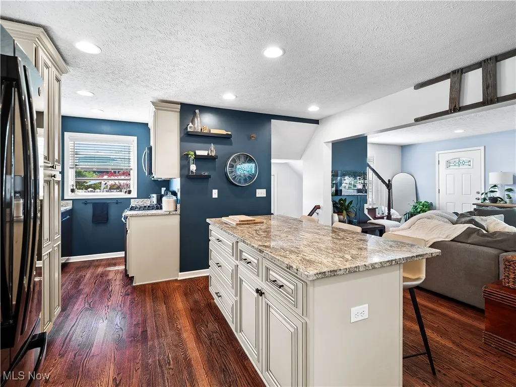 Kitchen featuring hardwood flooring, granite counters, cream colored cabinets, and huge island