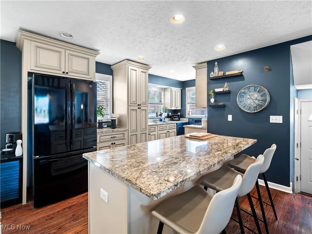Kitchen featuring hardwood flooring, granite counters, cream colored cabinets, and huge island