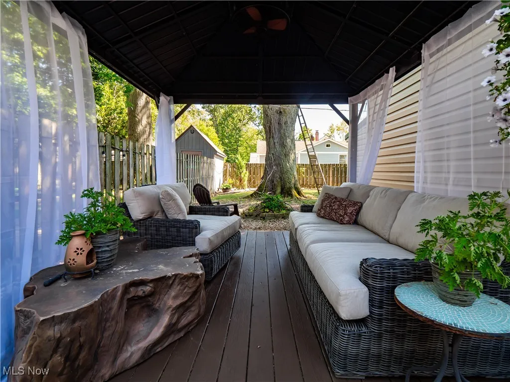Wooden terrace with a cozy outdoor hangout area, a fenced backyard, a gazebo, and an outbuilding