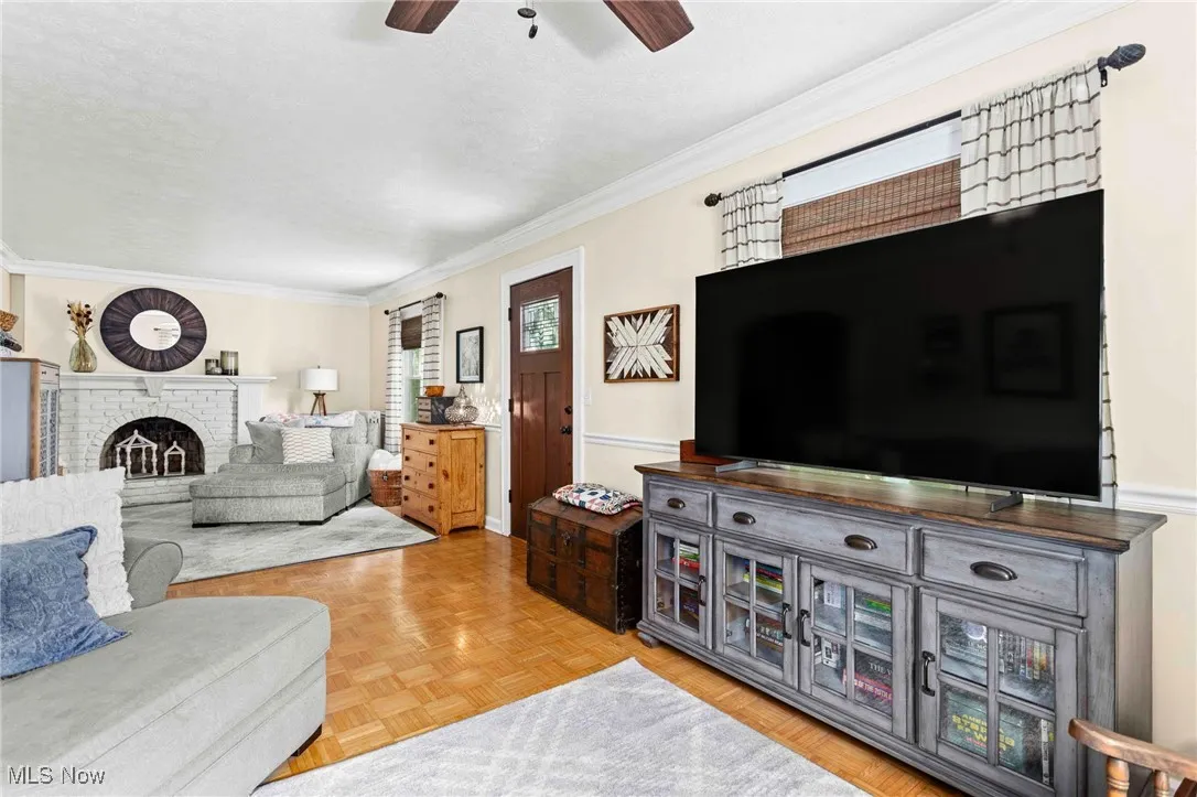 Living area with a ceiling fan, a textured ceiling, crown molding, and a brick fireplace