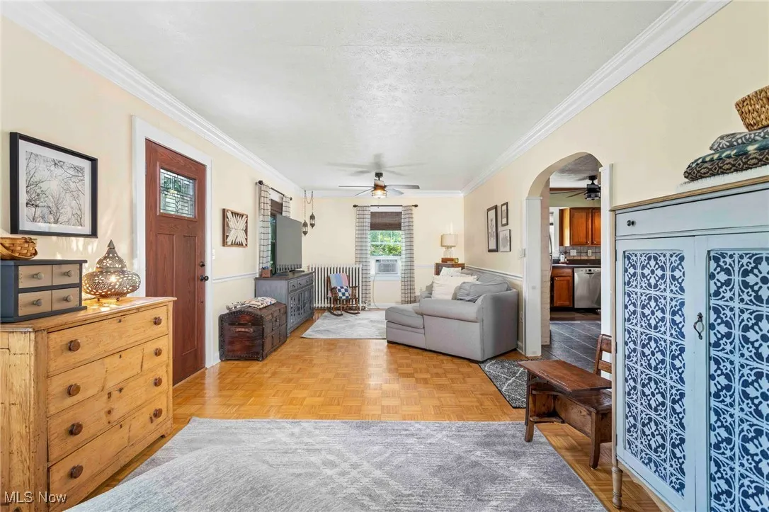 Living area featuring a ceiling fan, a textured ceiling, arched walkways, and crown molding