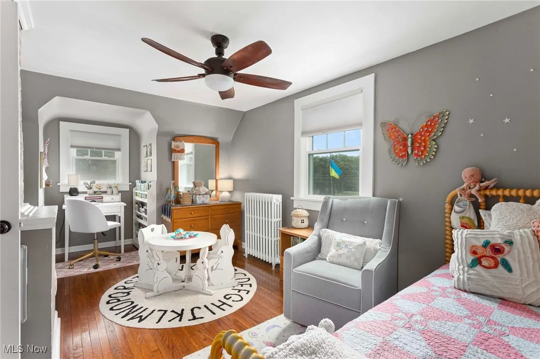 Bedroom featuring hardwood / wood-style flooring, radiator heating unit, multiple windows, and ceiling fan