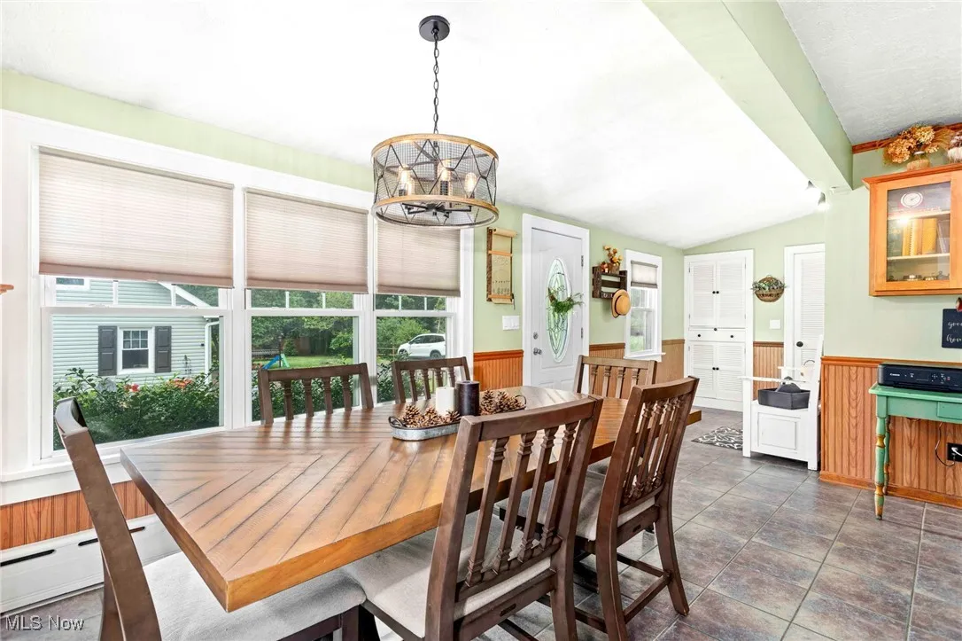 Tiled dining space featuring wainscoting, wooden walls, a chandelier, a baseboard heating unit, and vaulted ceiling