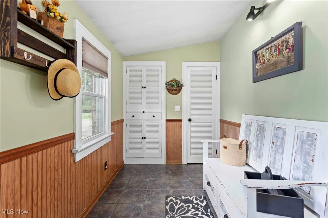 Mudroom with wainscoting, wooden walls, and lofted ceiling