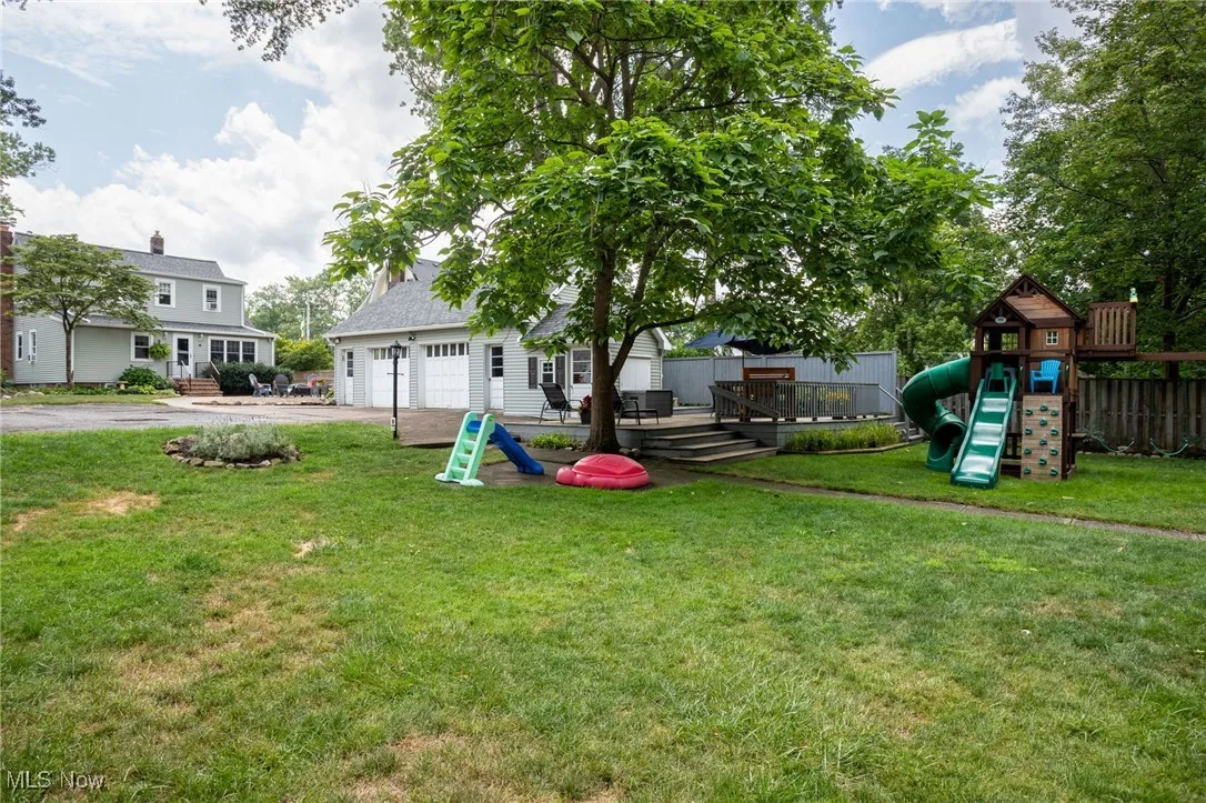 View of grassy yard featuring a garage, a playground, driveway, and a​​‌​​​​‌​​‌‌​‌‌​​​‌‌​‌​‌​‌​​​‌​​ deck