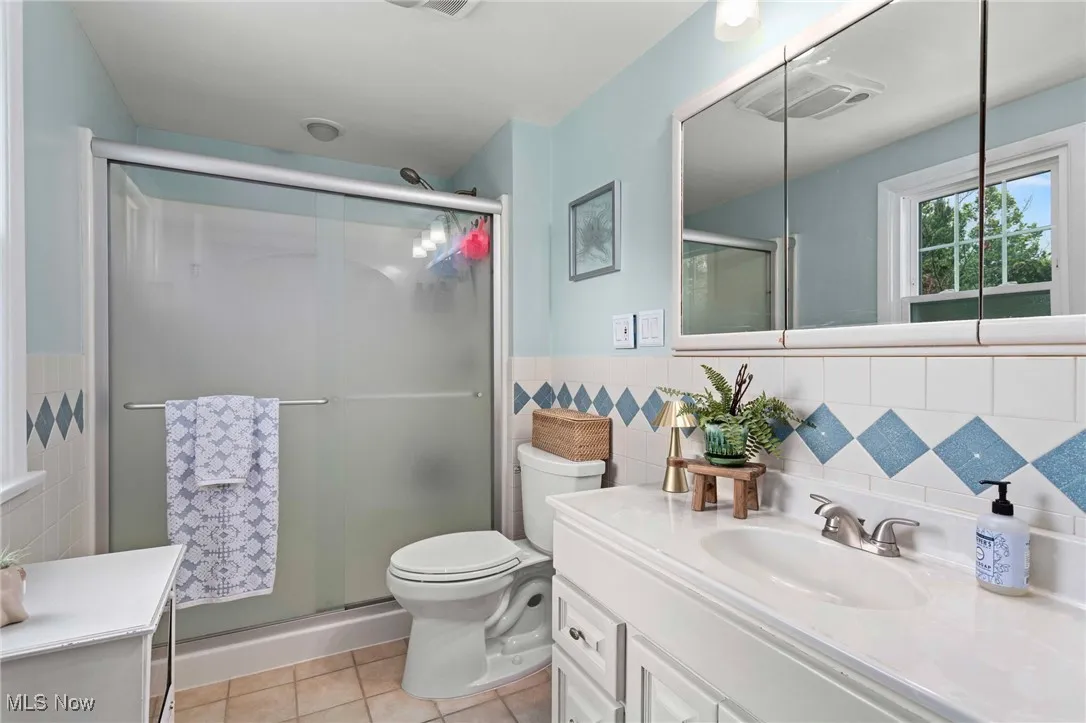Bathroom featuring tile walls, tile patterned floors, vanity, a wainscoted wall, and a shower stall