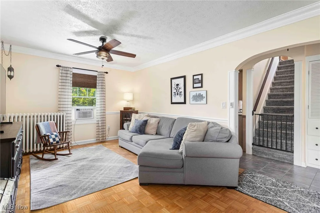 Living area with ornamental molding, arched walkways, a ceiling fan, a textured ceiling, and radiator
