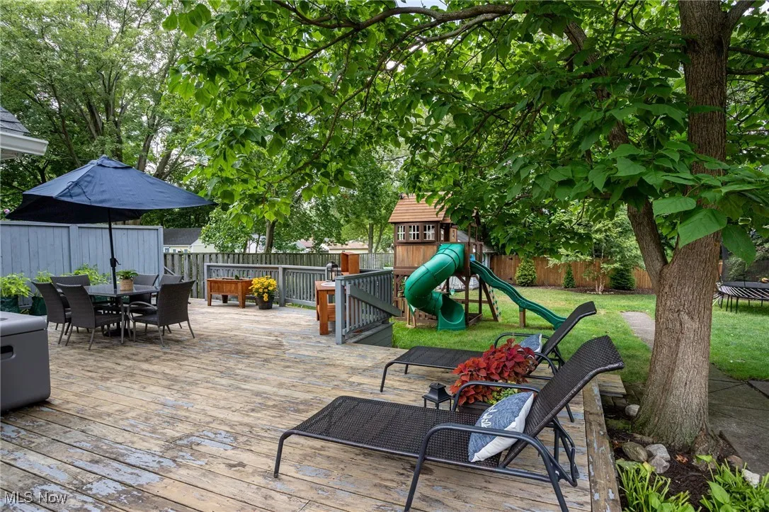 Wooden deck featuring outdoor dining area, a fenced backyard, and a playground