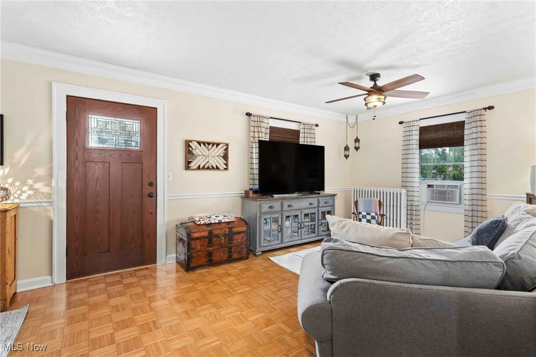 Living room featuring ornamental molding, ceiling fan, a textured ceiling, and radiator heating unit