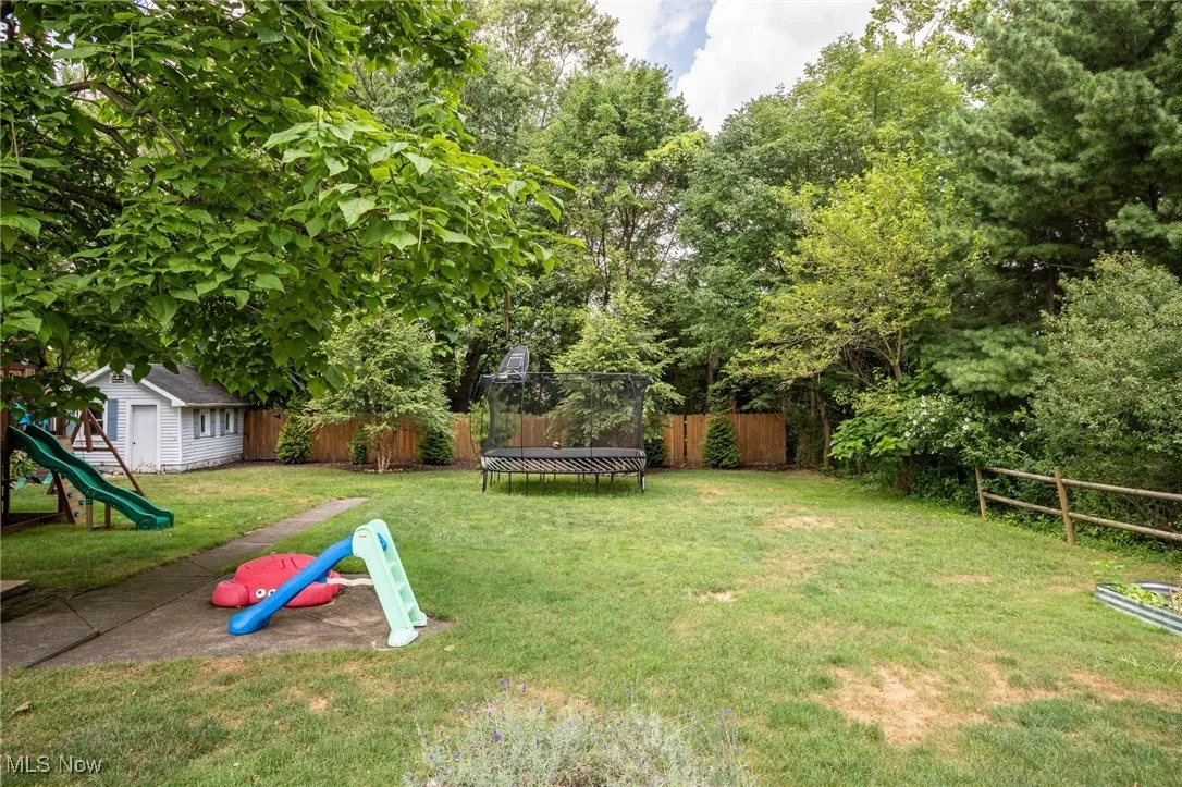 Fenced backyard with a trampoline, a playground, and a storage shed