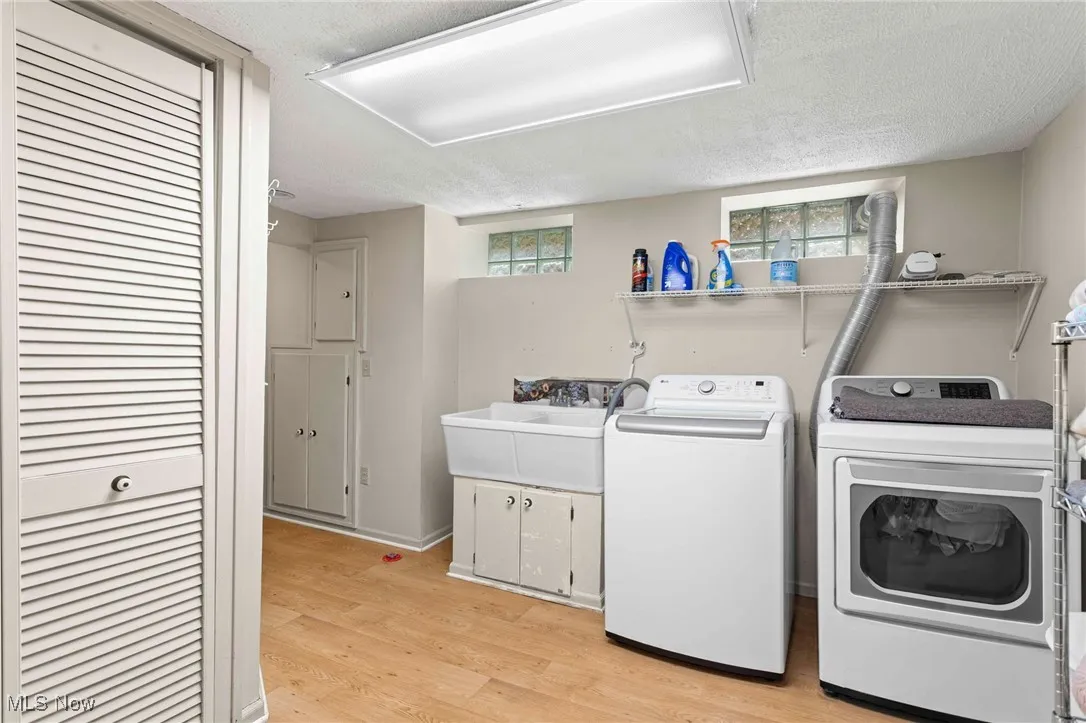 Laundry area with washing machine and clothes dryer, a textured ceiling, plenty of natural light, and light wood-style floors