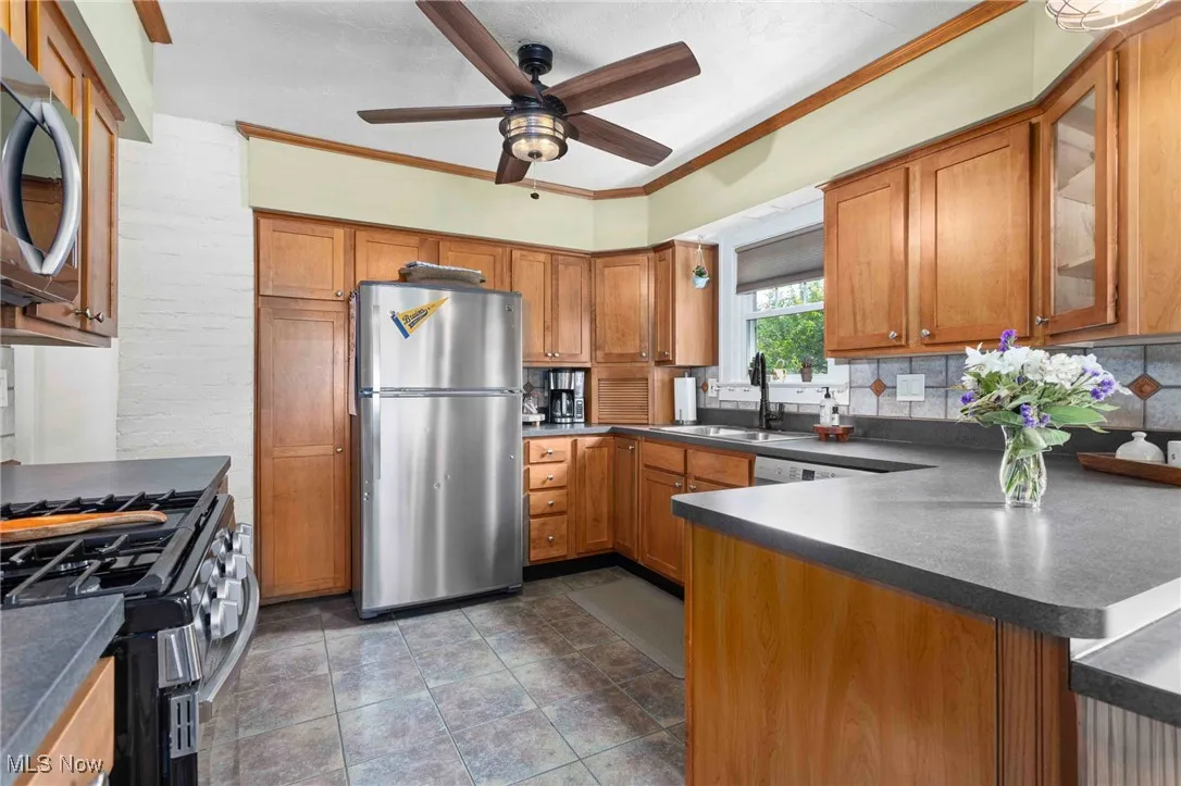 Kitchen with appliances with stainless steel finishes, a ceiling fan, brown cabinetry, backsplash, and crown molding