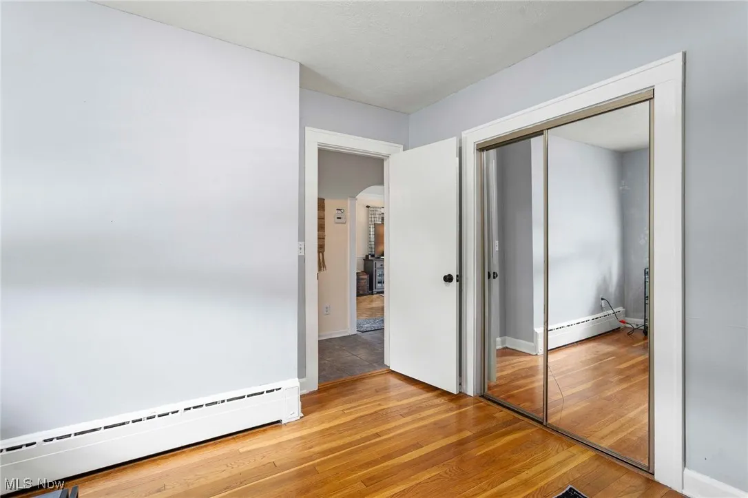 Unfurnished bedroom featuring a baseboard heating unit, light wood finished floors, arched walkways, and a closet