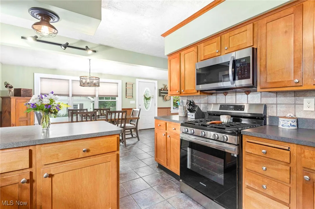 Kitchen featuring appliances with stainless steel finishes, light tile patterned flooring, dark countertops, a wainscoted wall, and a chandelier