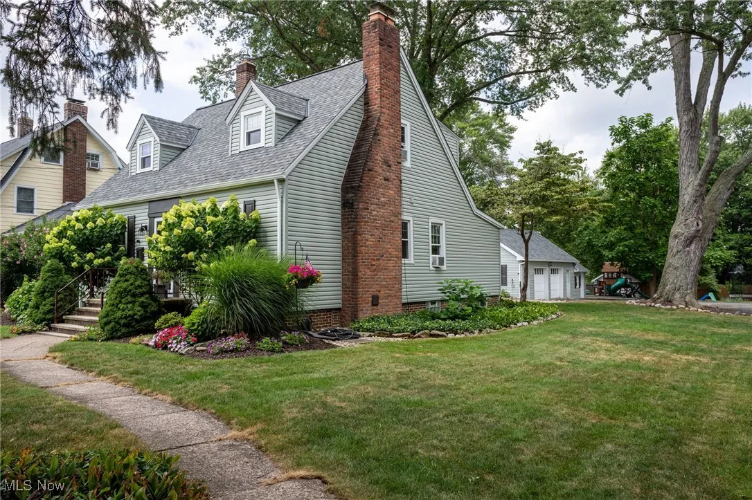 View of home's exterior with a chimney, a lawn, roof with shingles, and a detached garage
