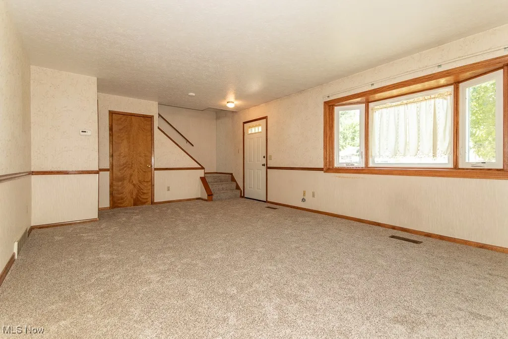 Living room with stairway, wallpapered walls, and a textured ceiling