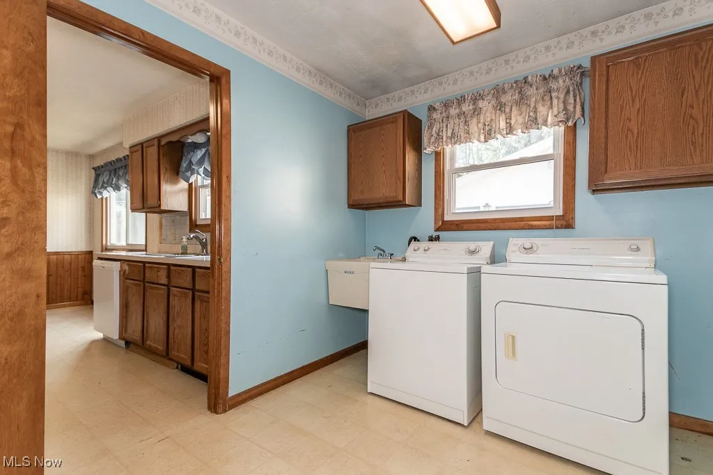 Washroom featuring light flooring, washing machine and clothes dryer, cabinet space, and wallpapered walls