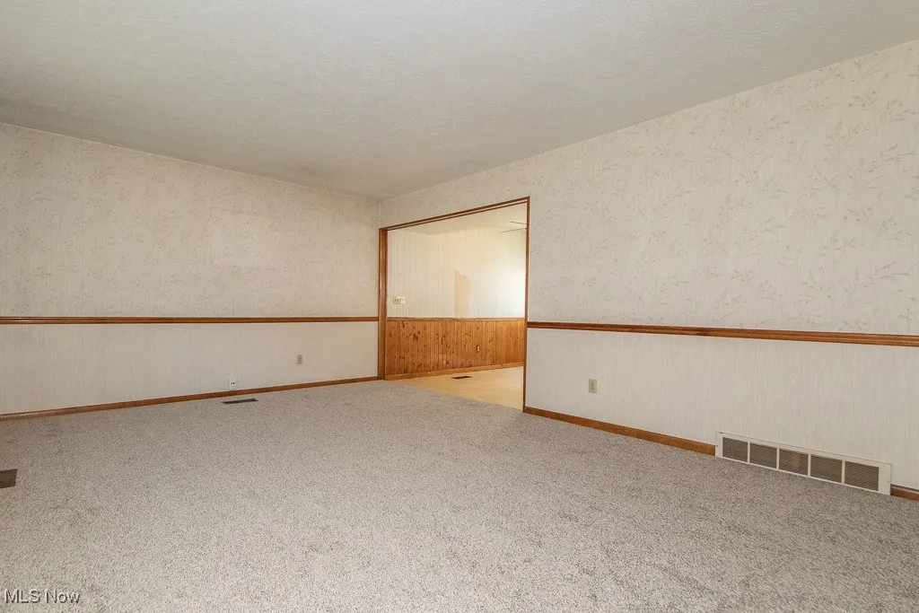 Living room featuring wallpapered walls, a textured ceiling, and a wainscoted wall