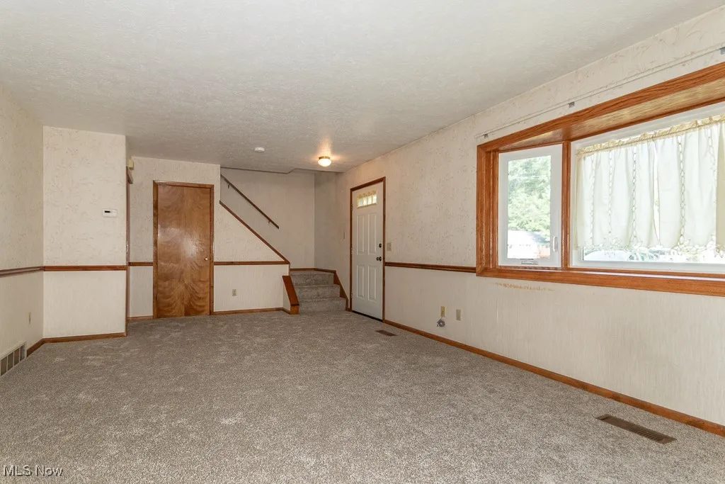 Carpeted living room with wallpapered walls, stairway, and a textured ceiling