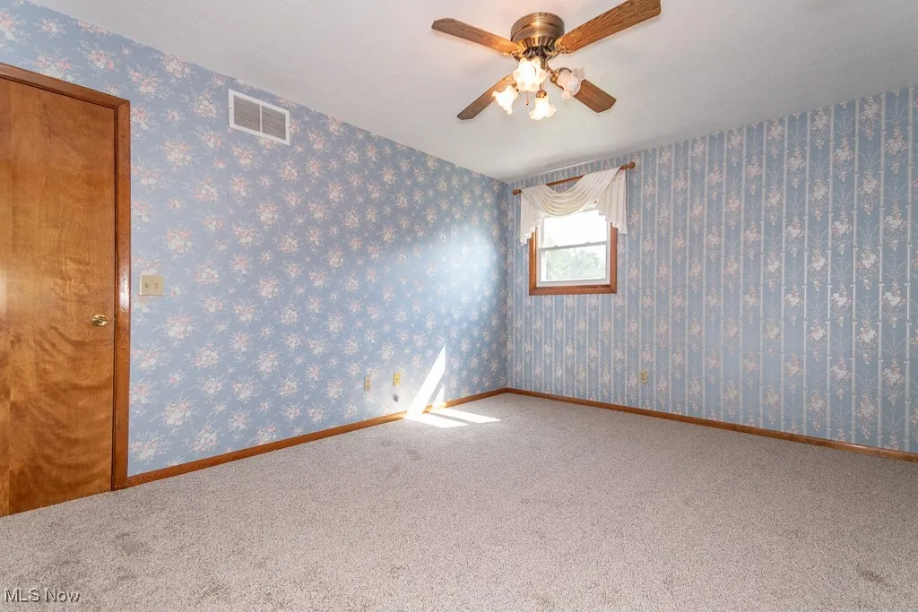 Carpeted empty room with a ceiling fan and wallpapered walls