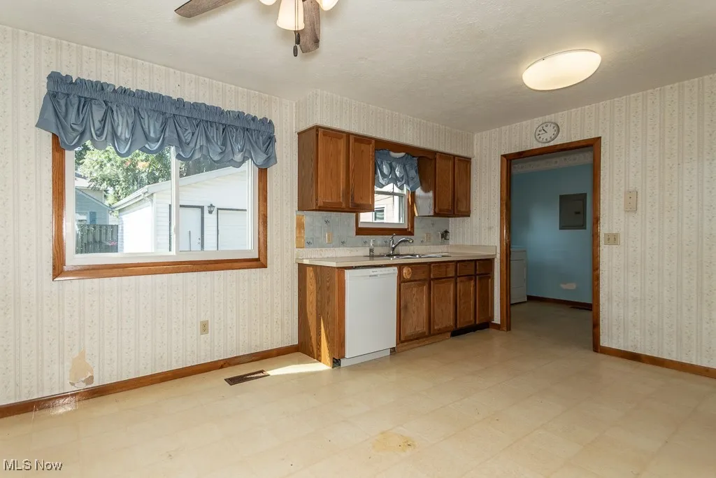 Kitchen with wallpapered walls, light countertops, light floors, brown cabinets, and plenty of natural light
