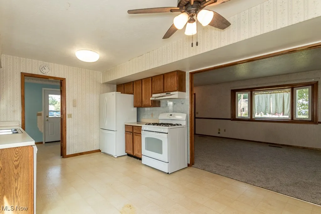 Kitchen with wallpapered walls, light flooring, white appliances, brown cabinetry, and light countertops