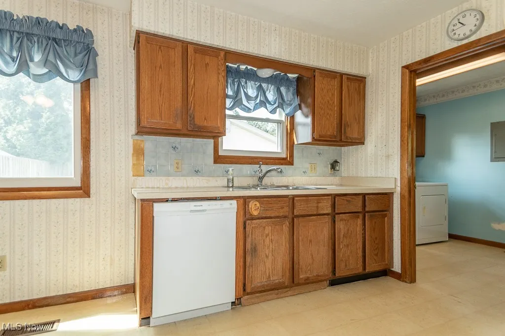 Kitchen featuring light floors, brown cabinets, wallpapered walls, light countertops, and dishwasher