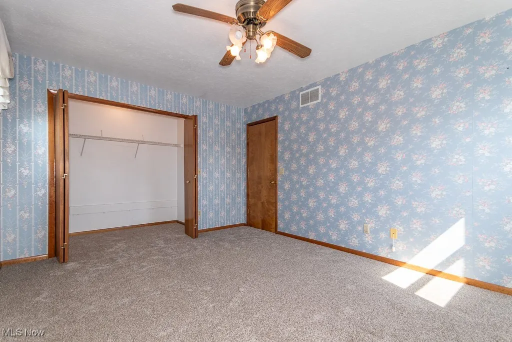 Unfurnished bedroom with wallpapered walls, carpet floors, a ceiling fan, a closet, and a textured ceiling