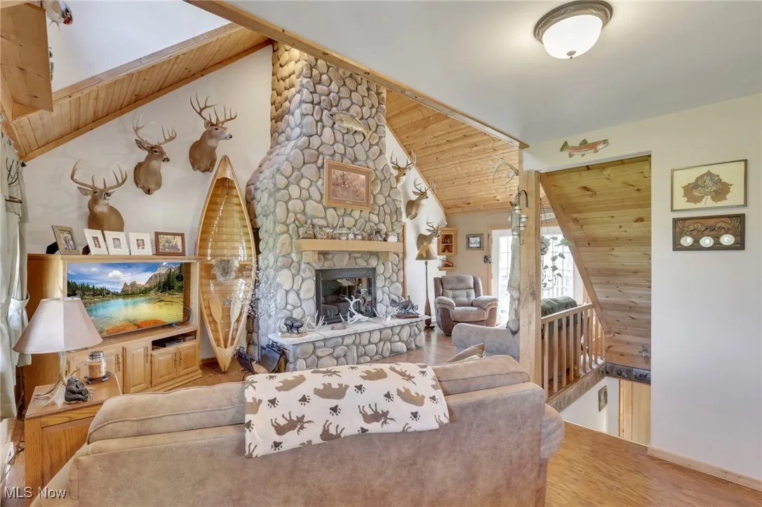 Living room featuring wood ceiling, wood finished floors, a stone fireplace, and high vaulted ceiling