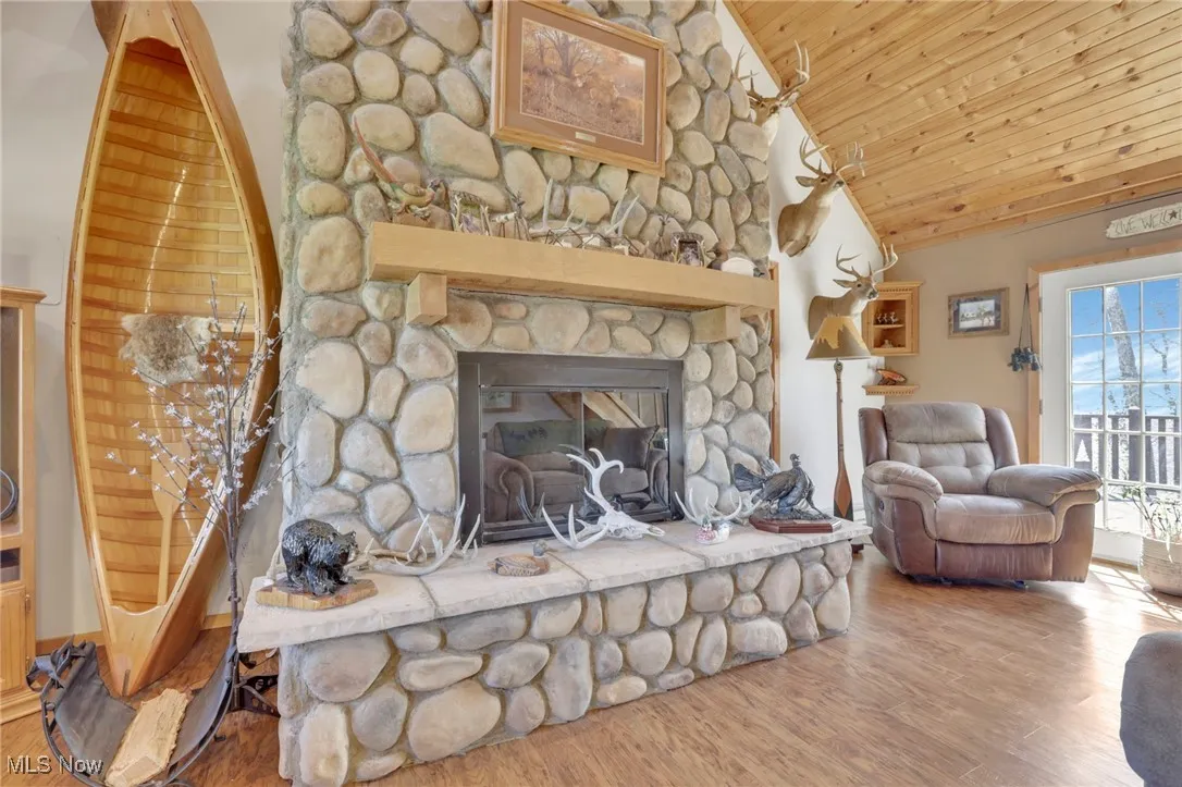 Living room featuring wood finished floors, a stone fireplace, high vaulted ceiling, and wooden ceiling